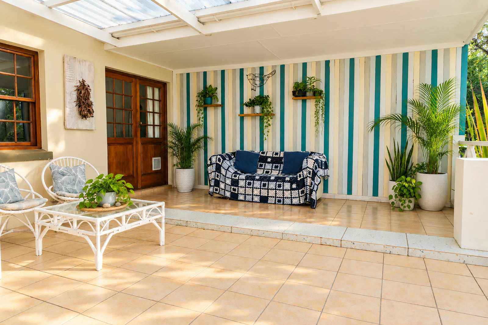 Covered patio at Sunbird Chalet with shaded seating, potted plants and the entrance doors