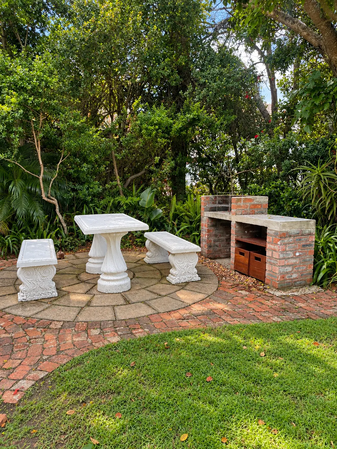 Garden braai at Fish Eagle Chalet with a brick barbecue, white garden table and benches on a brick patio among trees