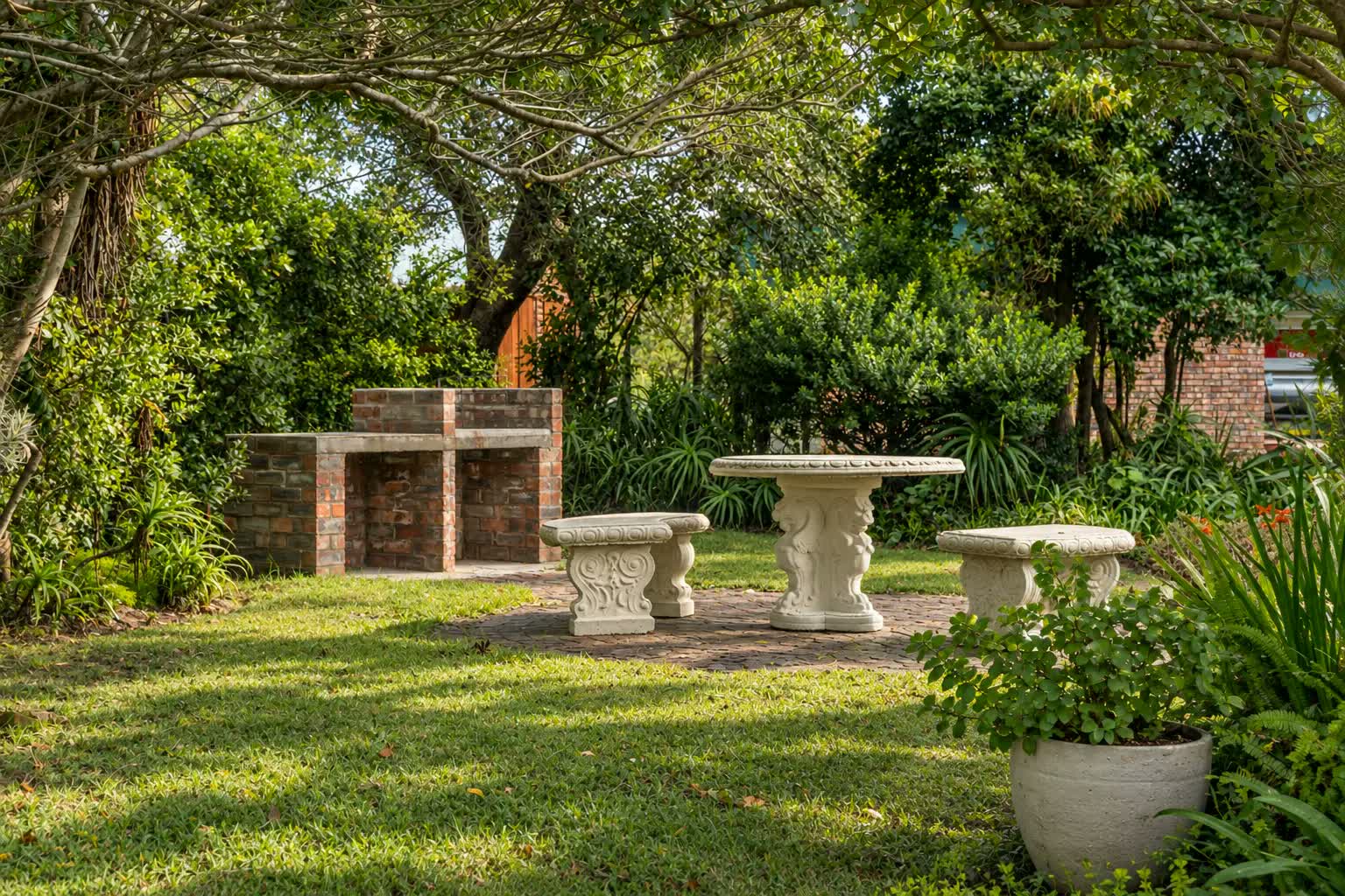 Loerie Chalet garden with a built-in brick braai and a carved stone table and benches on a sunlit paved patio