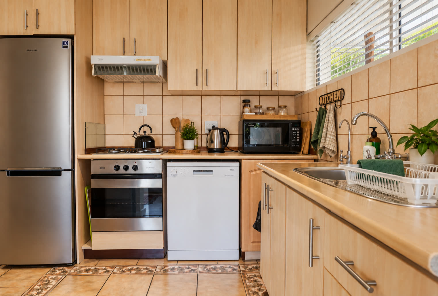 Loerie Chalet kitchen with light wood cabinets, a stainless steel fridge, a built-in oven and stovetop, a dishwasher, a microwave and a sink beneath a window with blinds