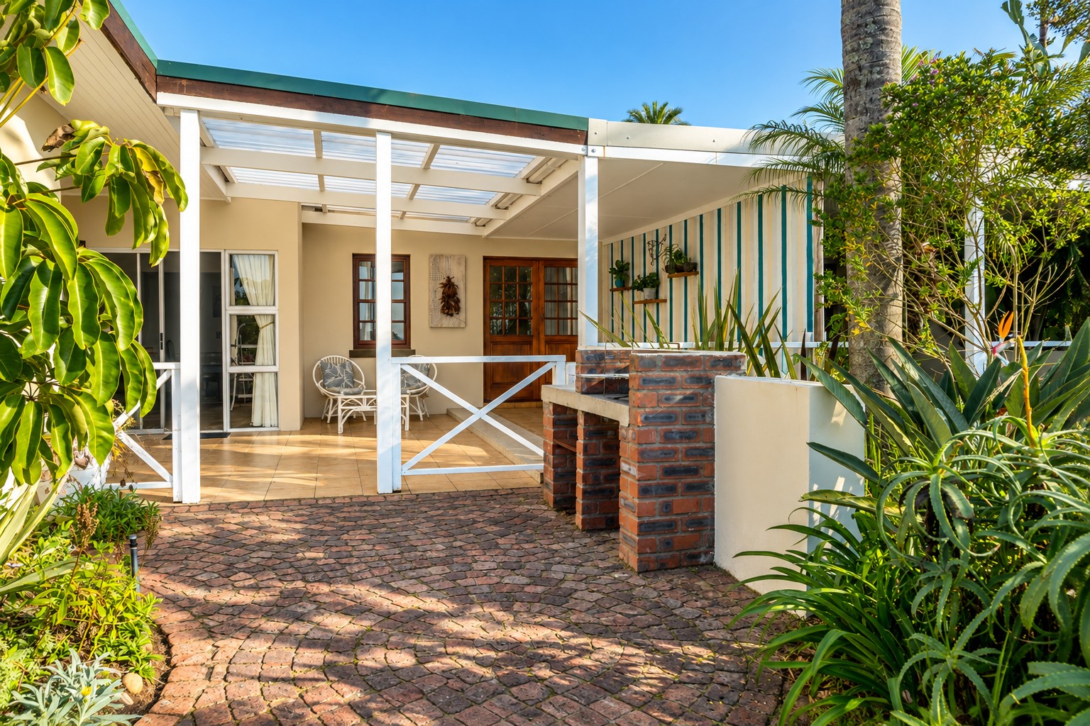 Covered patio at Sunbird Chalet with shaded seating, a braai and the entrance doors under a pergola
