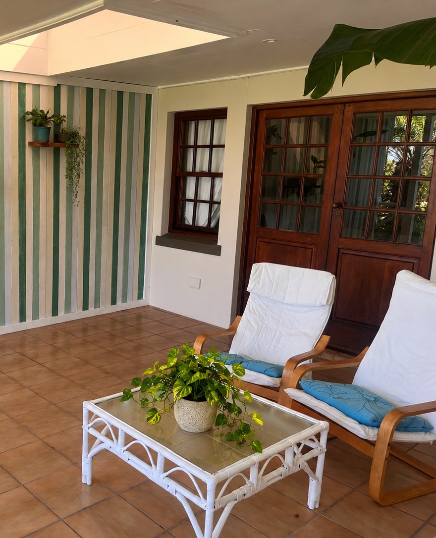 Sunlit stoep at Fish Eagle Chalet with two wooden armchairs, a glass-topped table and a striped timber feature wall under a skylight